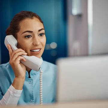 Nurse answering a phone in front of a computer at a desk in a medical office.