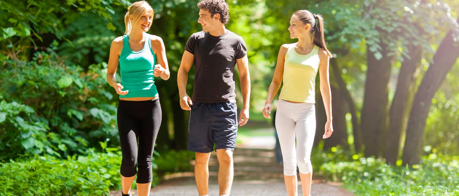 2 women and a man walking on a trail with trees in the background