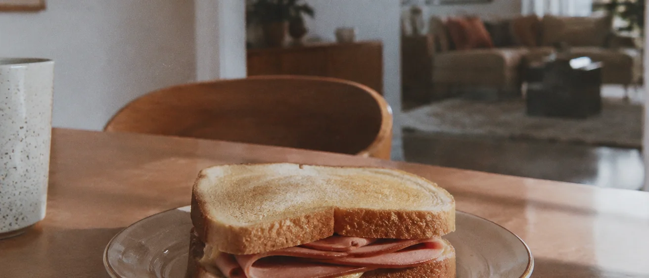 A plated bologna sandwich sitting on a wooden dining table