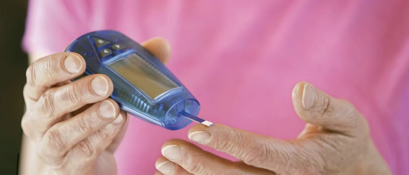 patient in pink shirt self-administering glucose metering test on finger