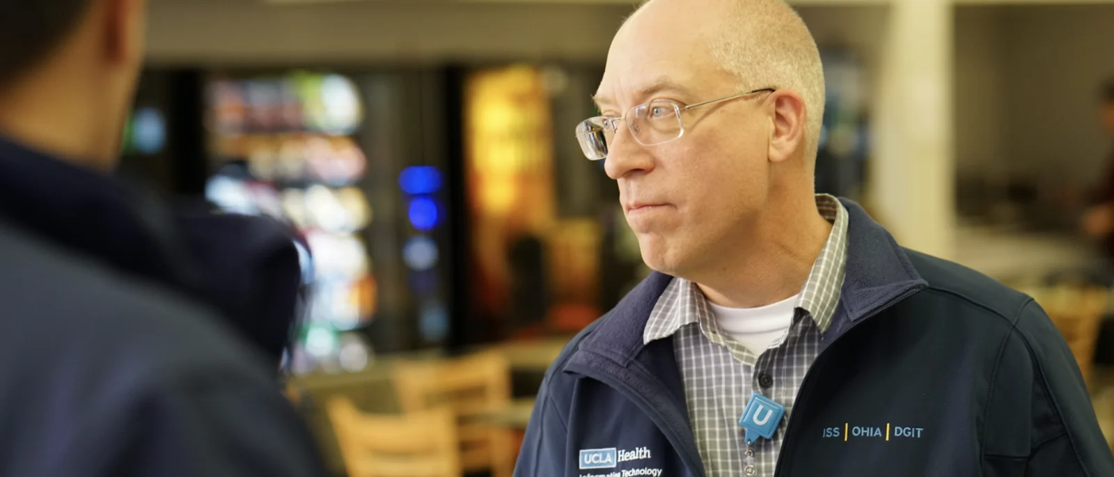 Man looking to the left with glasses and wearing a UCLA Health IT Jacket