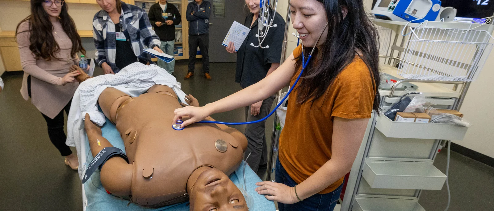 Woman in orange shirt interacts with simulation dummy