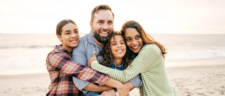 A family of four smiling and hugging on a beach