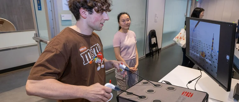 a student working with the invented device. he's using a monitor to see the location of the needles.