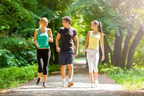 2 women and a man walking on a trail with trees in the background