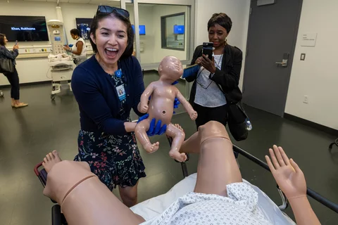 A lady, smiling and holding a simulation baby doll at the Simulation Center. This simulation is one of childbirth.