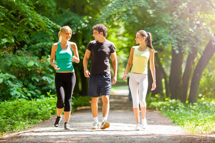 2 women and a man walking on a trail with trees in the background