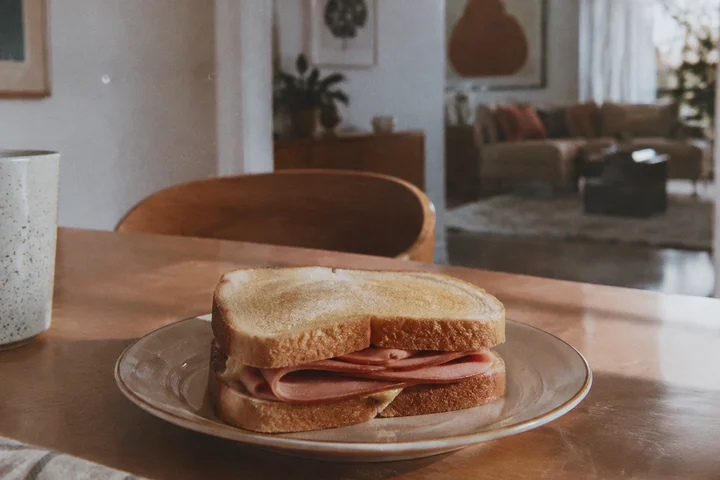 A plated bologna sandwich sitting on a wooden dining table