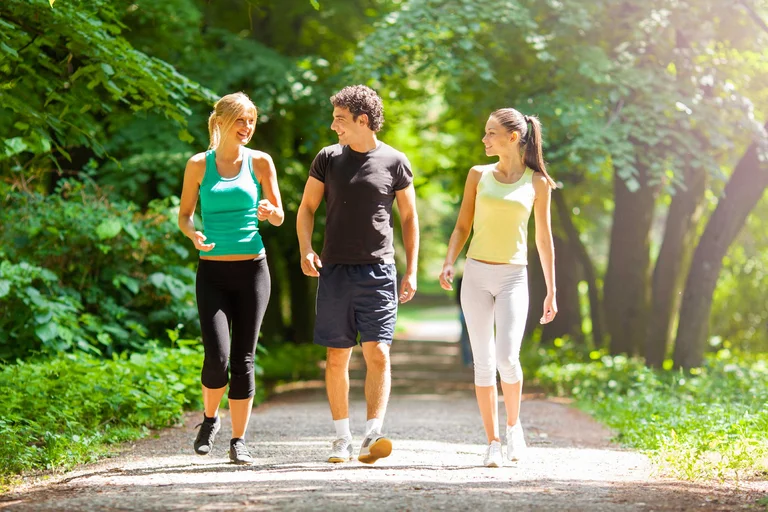 2 women and a man walking on a trail with trees in the background