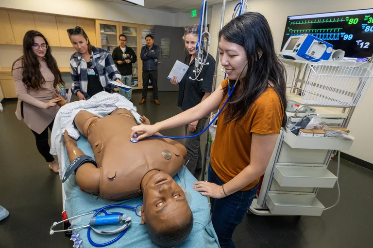 Woman in orange shirt interacts with simulation dummy