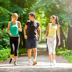 2 women and a man walking on a trail with trees in the background
