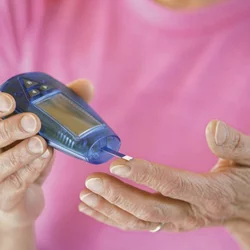 patient in pink shirt self-administering glucose metering test on finger