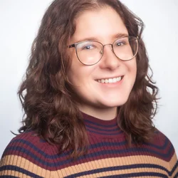 Image of a white woman with brown wavy hair and glasses wearing a striped shirt on a white background.