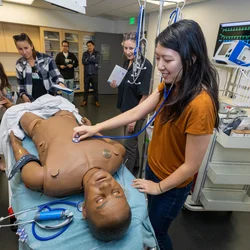 Woman in orange shirt interacts with simulation dummy