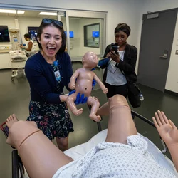 A lady, smiling and holding a simulation baby doll at the Simulation Center. This simulation is one of childbirth.