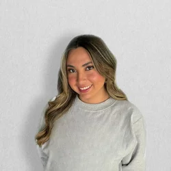 photo of someone standing and smiling with a grey sweater and white background