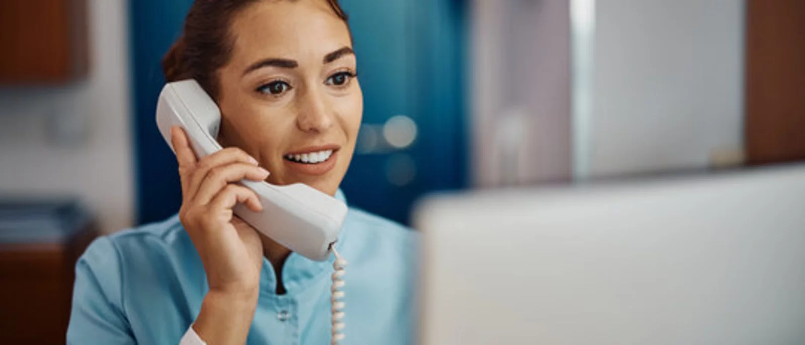 Nurse answering a phone in front of a computer at a desk in a medical office.