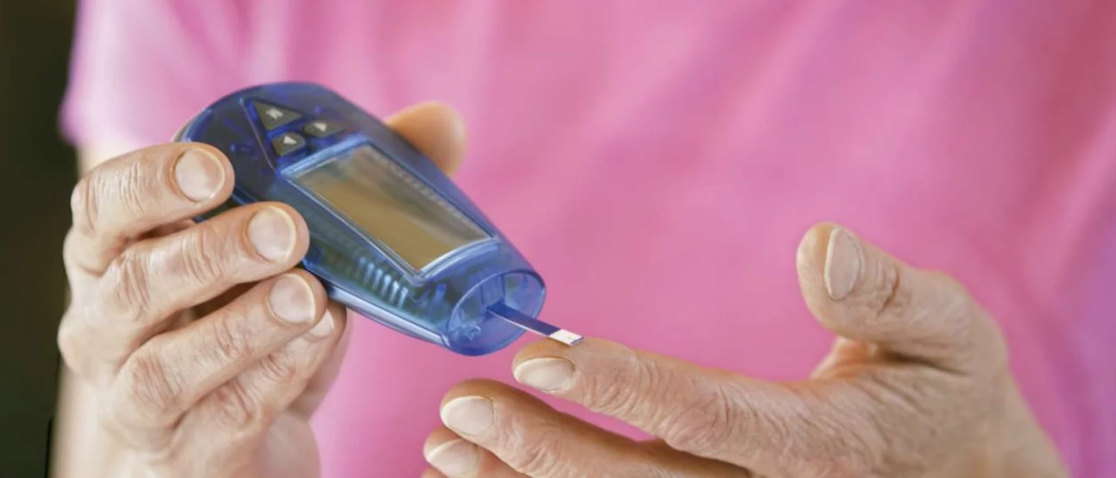 patient in pink shirt self-administering glucose metering test on finger
