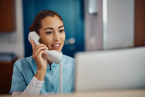 Nurse answering a phone in front of a computer at a desk in a medical office.
