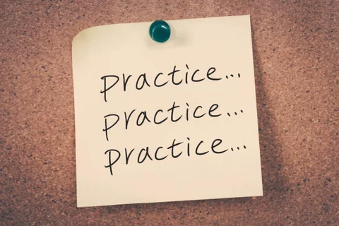 Yellow sticky note with word practice followed by ellipsis written three times. The sticky note is tacked onto a corkboard background with a green pin..