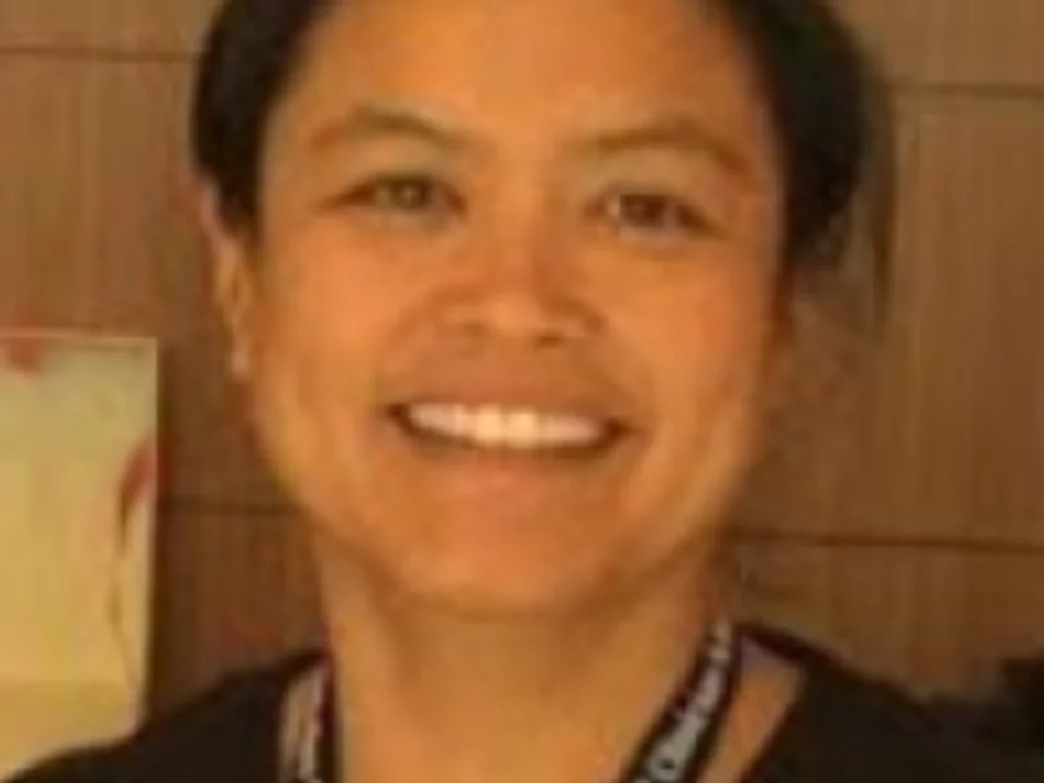 Filipina American Women with black hair, smile and lanyard. Background is wood panel